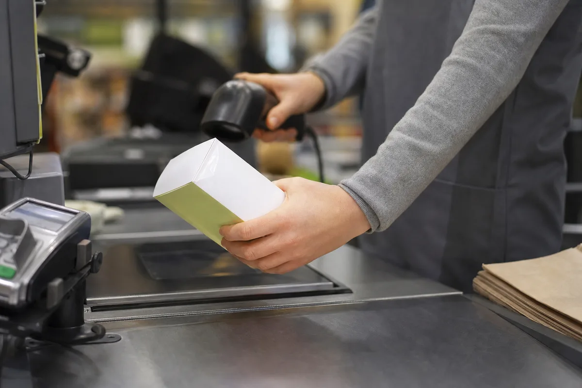 Mains d&rsquo;un employé scannant un article à une caisse enregistreuse de magasin